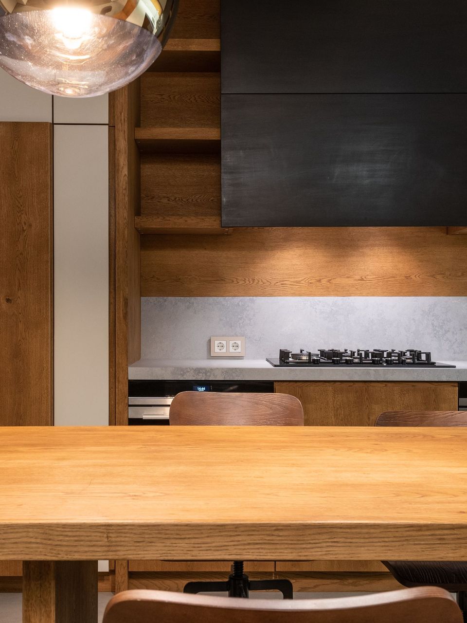 Mesa de madeira maciça diante da cozinha, com prateleiras e pendente
