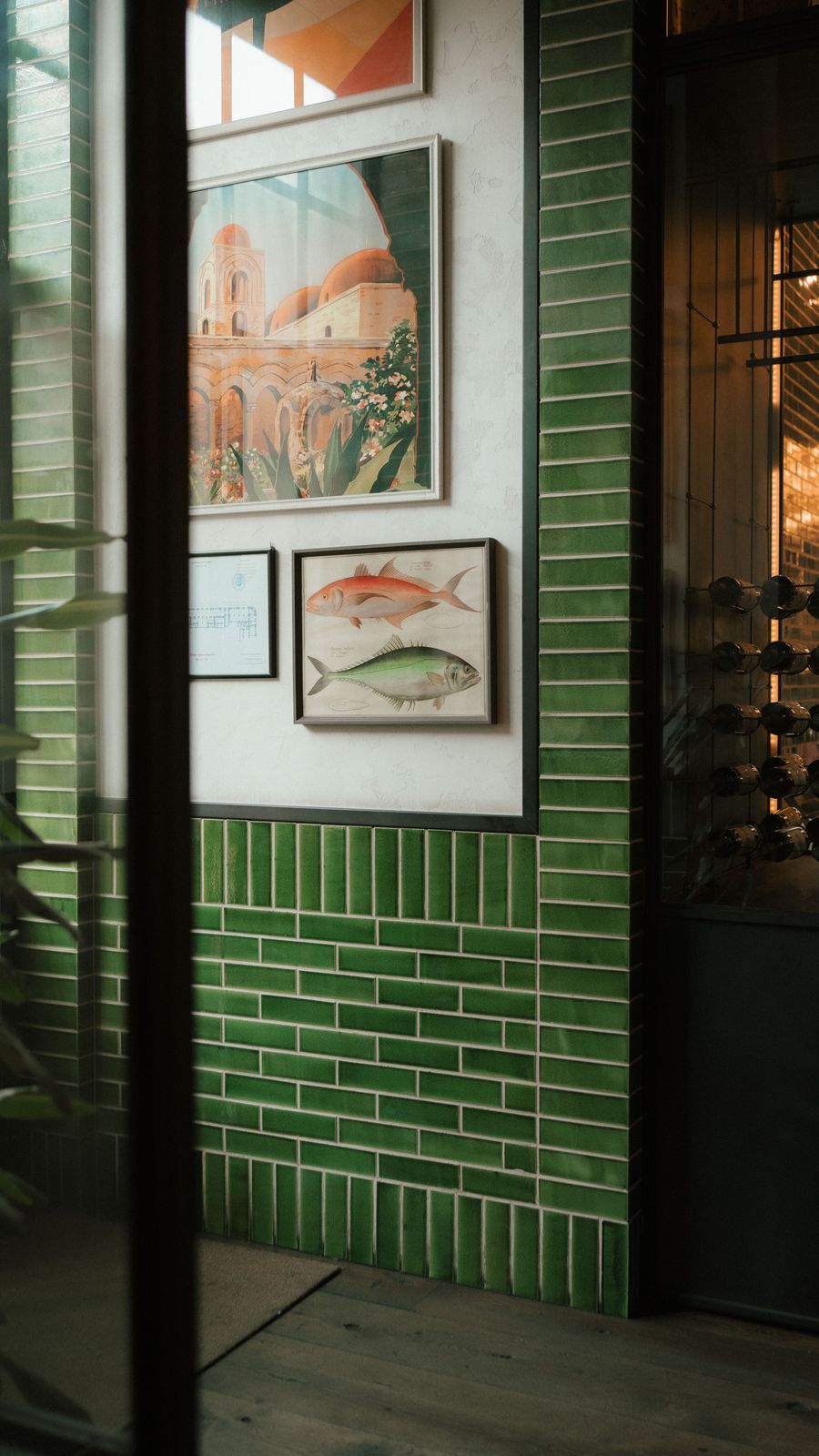 Parede em azulejo verde com quadros emoldurados e uma adega de porta de vidro
