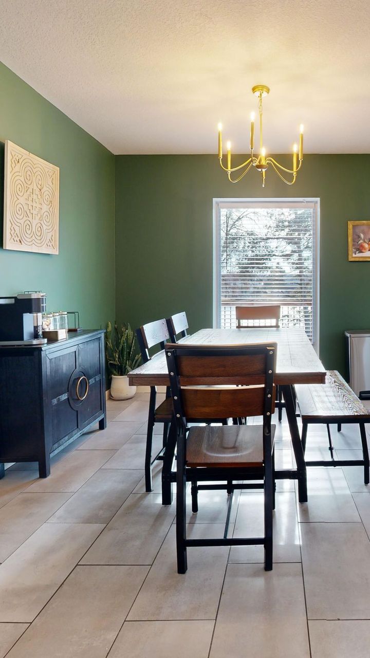 Sala de jantar com parede verde, mesa de madeira e lustre dourado